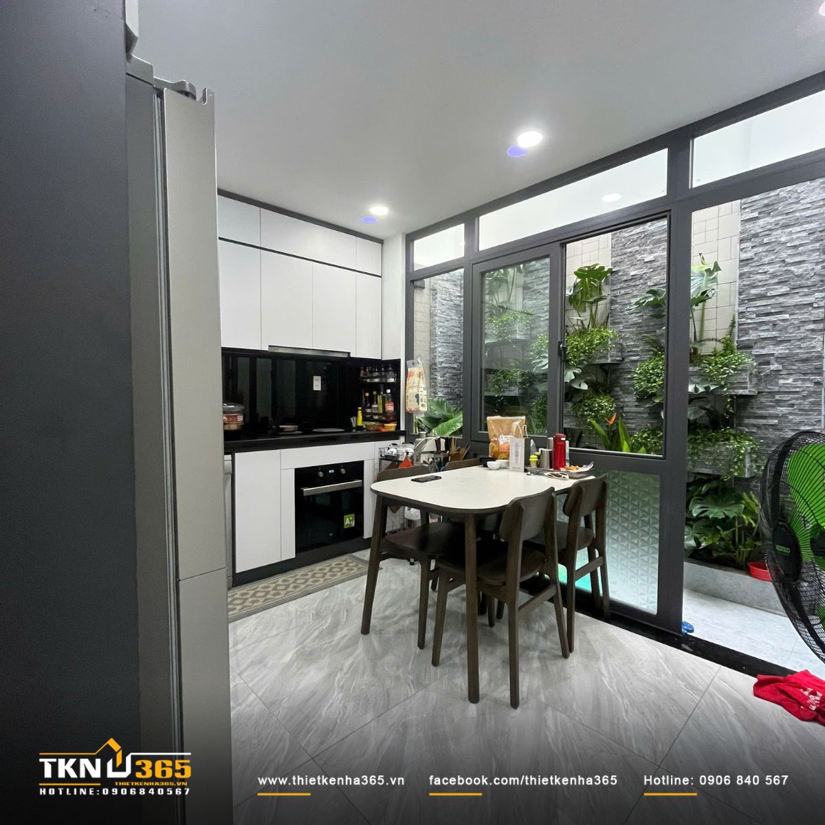 Bàn ăn đặt cạnh cửa sổ kính lớn, tạo sự kết nối tự nhiên giữa bếp và khu vườn xanh bên ngoài