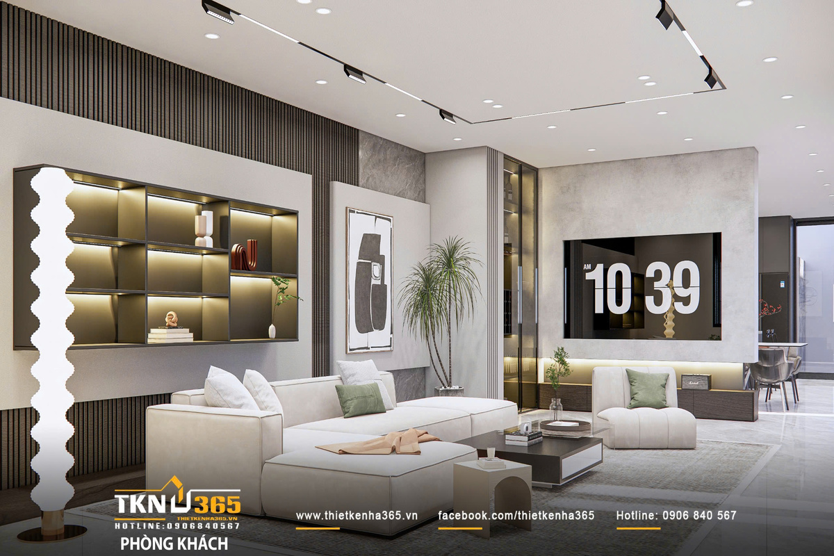 Bộ sofa dáng thấp cùng thảm lớn định hình khu vực sinh hoạt, trong khi hệ tủ âm tường với ánh sáng hắt tạo chiều sâu thị giác